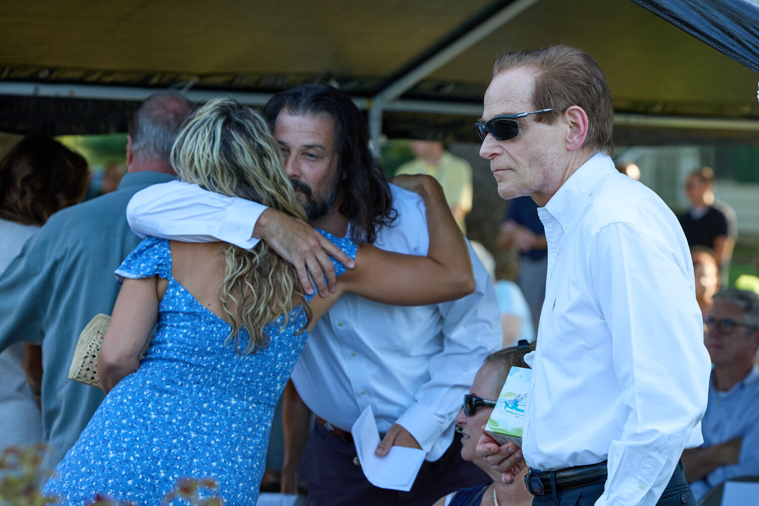 Zach DePiero, the son of flood victims Enzo and Linda DePiero, is comforted at Monday’s service as Dave Love, whose wife Yuko died in the flood, looks on.