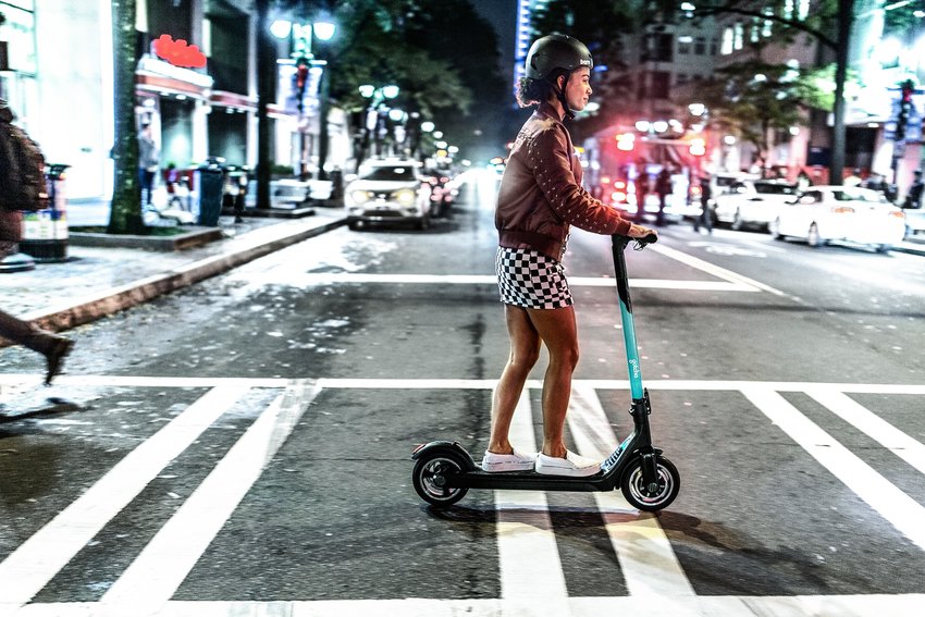 Promotional image of a woman riding a Gotcha scooter on a city cross-walk.